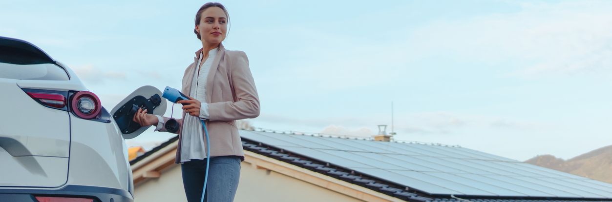 Femme qui recharge sa voiture électrique devant une maison
