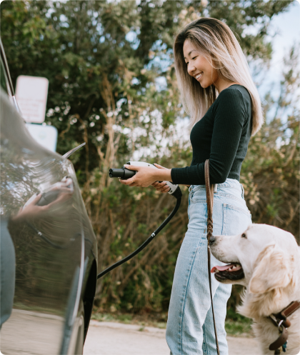 Femme rechargeant sa voiture électrique accompagnée de son chien.