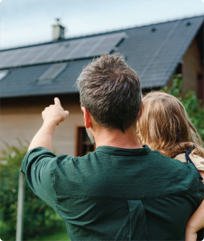 Père avec sa fille dans les bras devant une maison avec des panneaux photovoltaïques.