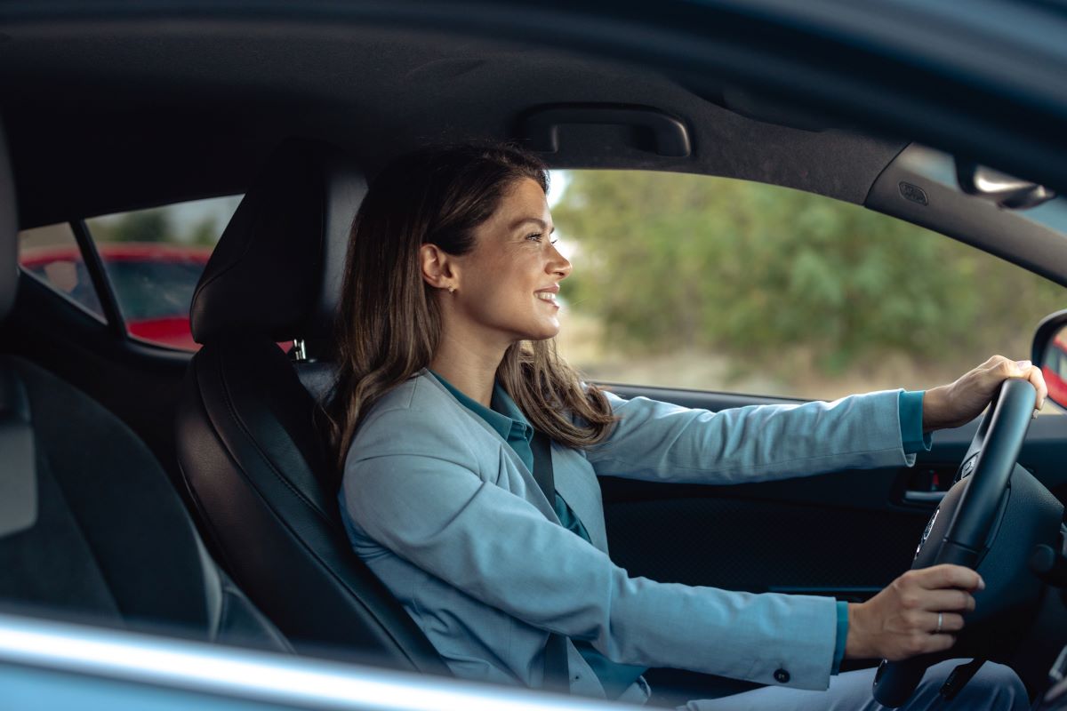 Femme souriante conduisant une voiture, vue de profil à l’intérieur du véhicule.