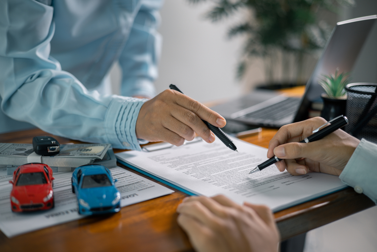 Signature d’un contrat de financement automobile avec documents et modèles de voitures.